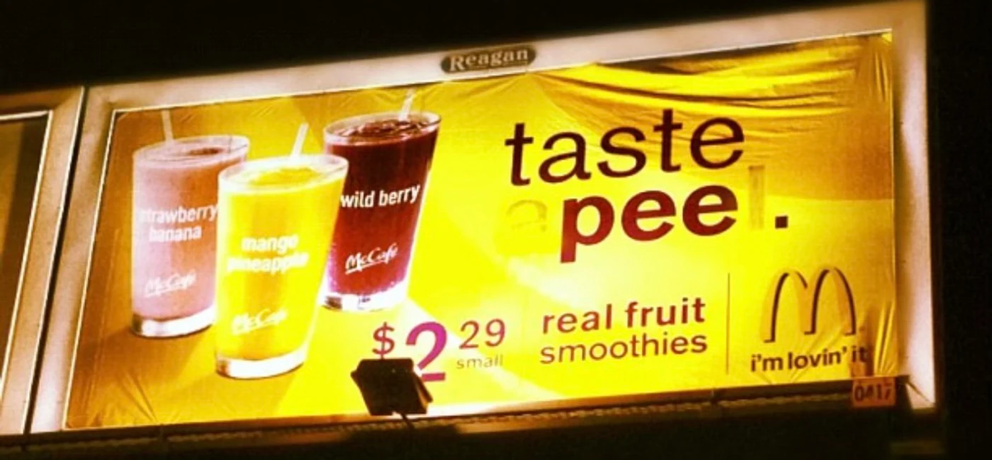 A McDonald's real fruit smoothies billboard at night, its headline altered by two letters covered in dark paint so it reads 'taste pee'.